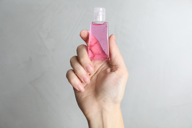 Woman holding antiseptic gel on light grey background, closeup