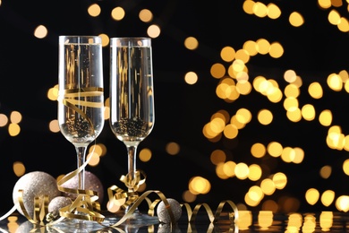 Glasses of champagne, Christmas decor and serpentine streamers against black background with blurred lights. Space for text