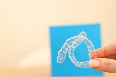 Photo of Woman with transparent dental aligners on blurred background, closeup. Space for text