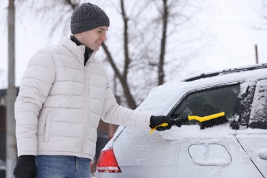 Photo of Man cleaning snow from car with brush outdoors