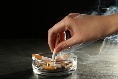 Woman extinguishing cigarette in glass ashtray
at grey table against black background, closeup