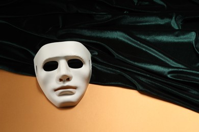 Photo of Theater arts. White mask and green fabric on pale orange background, above view