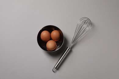 Photo of Metal whisk and raw eggs on grey background, flat lay
