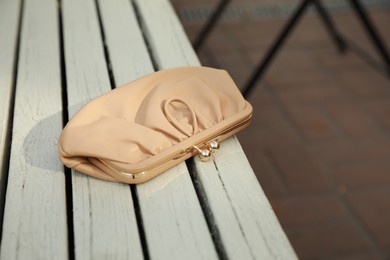Beige leather purse on wooden bench outdoors. Lost and found