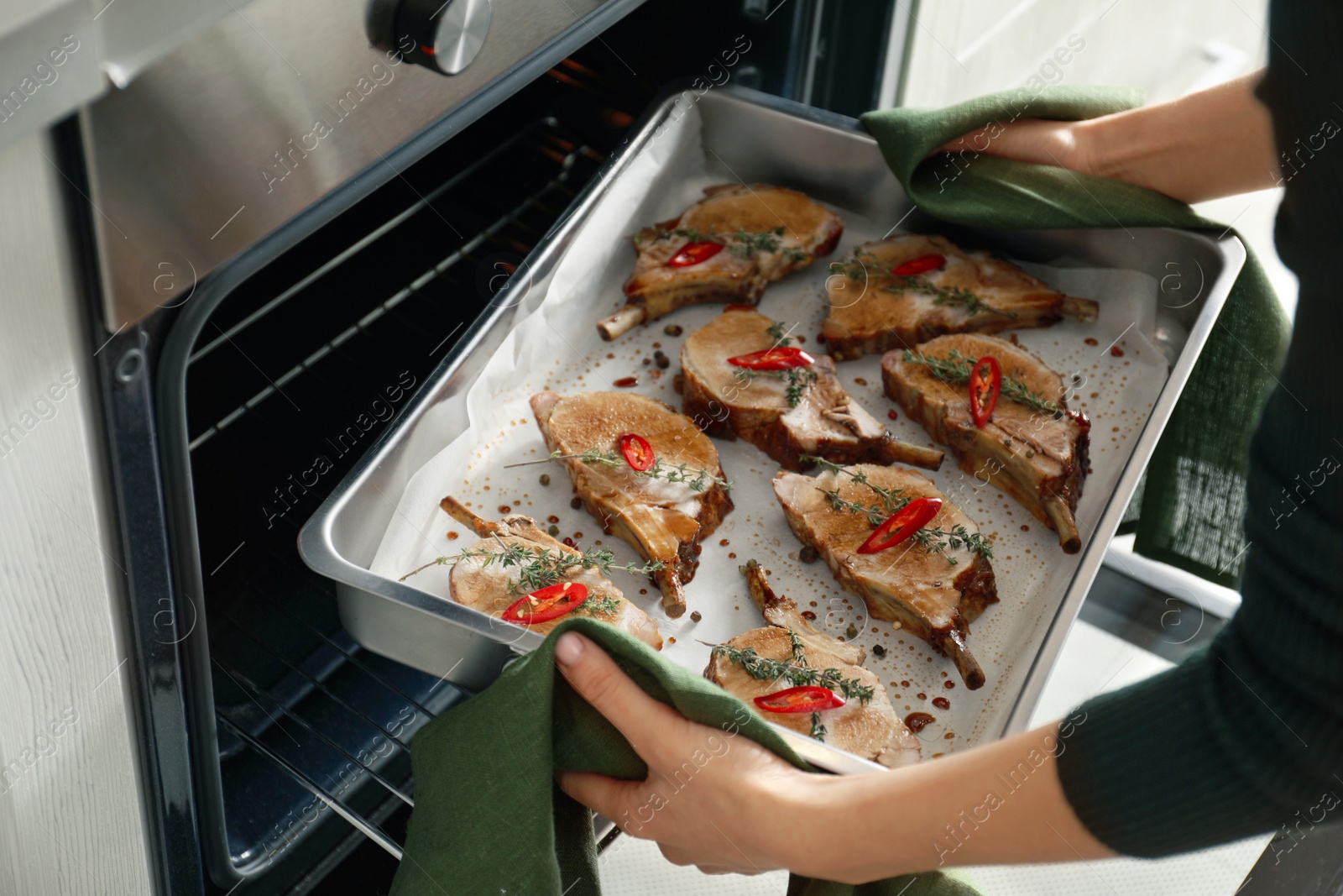 Photo of Woman taking delicious ribs out of oven, closeup