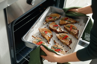 Woman taking delicious ribs out of oven, closeup