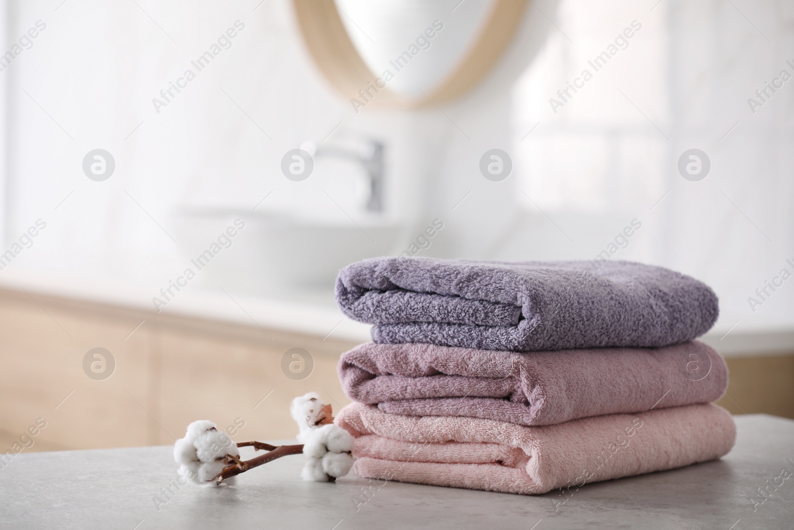 Photo of Stack of fresh towels and cotton flowers on table in bathroom