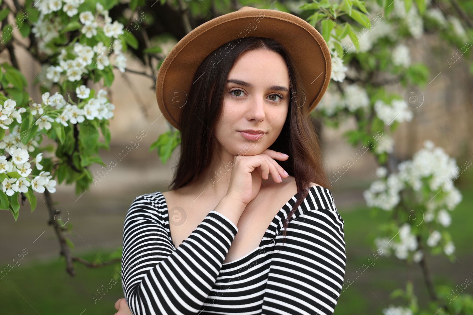 Photo of Beautiful woman in hat near blossoming tree on spring day