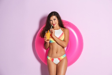 Beautiful young woman with inflatable ring and glass of cocktail on color background