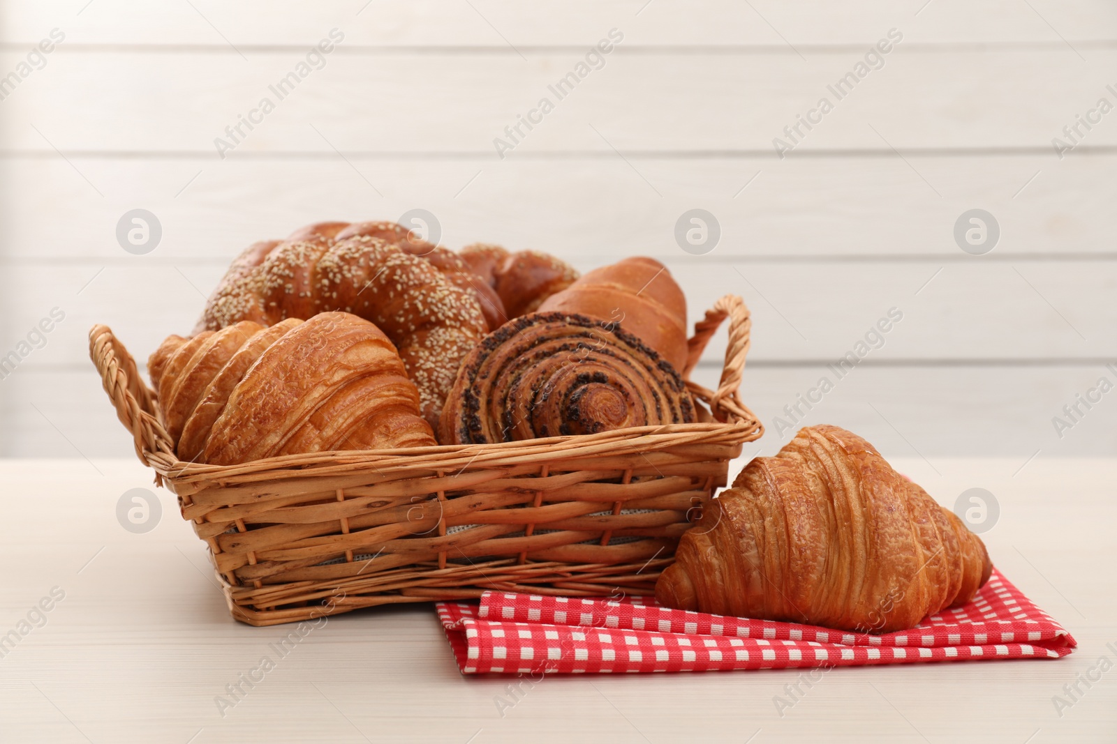 Photo of Wicker basket and different tasty freshly baked pastries on white table