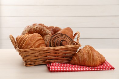 Photo of Wicker basket and different tasty freshly baked pastries on white table