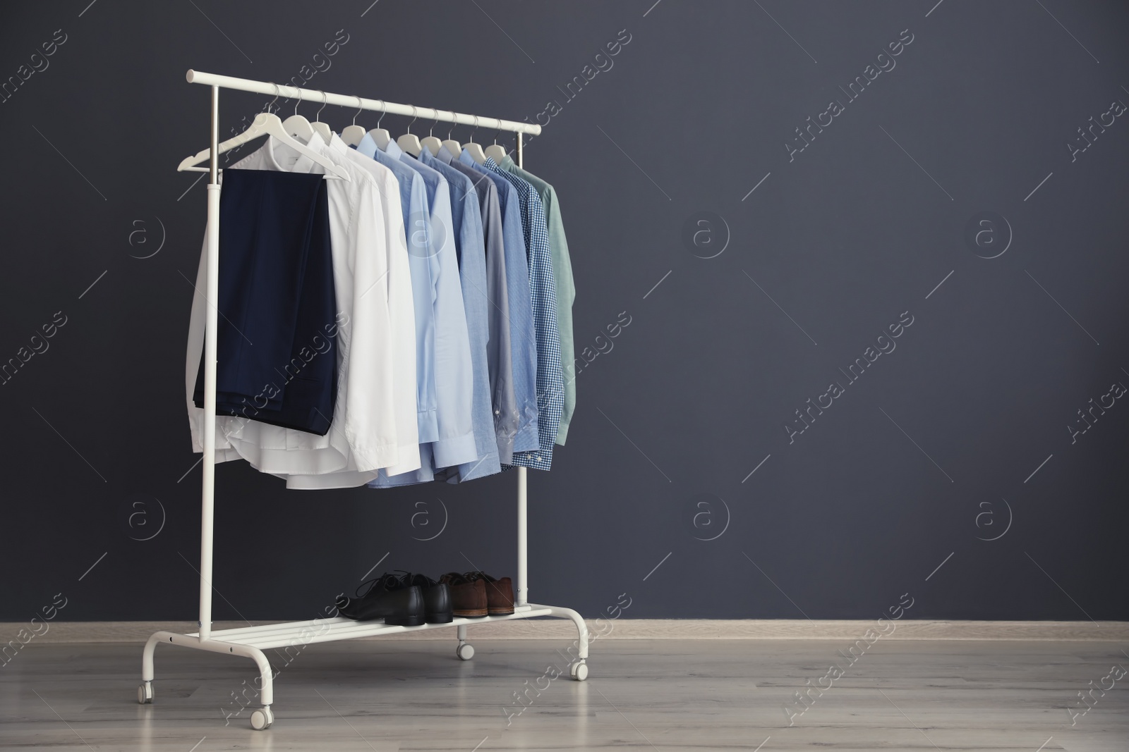 Photo of Wardrobe rack with men's clothes near grey wall. Space for text