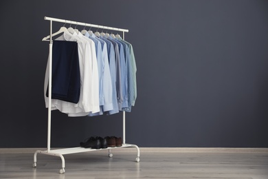 Photo of Wardrobe rack with men's clothes near grey wall. Space for text