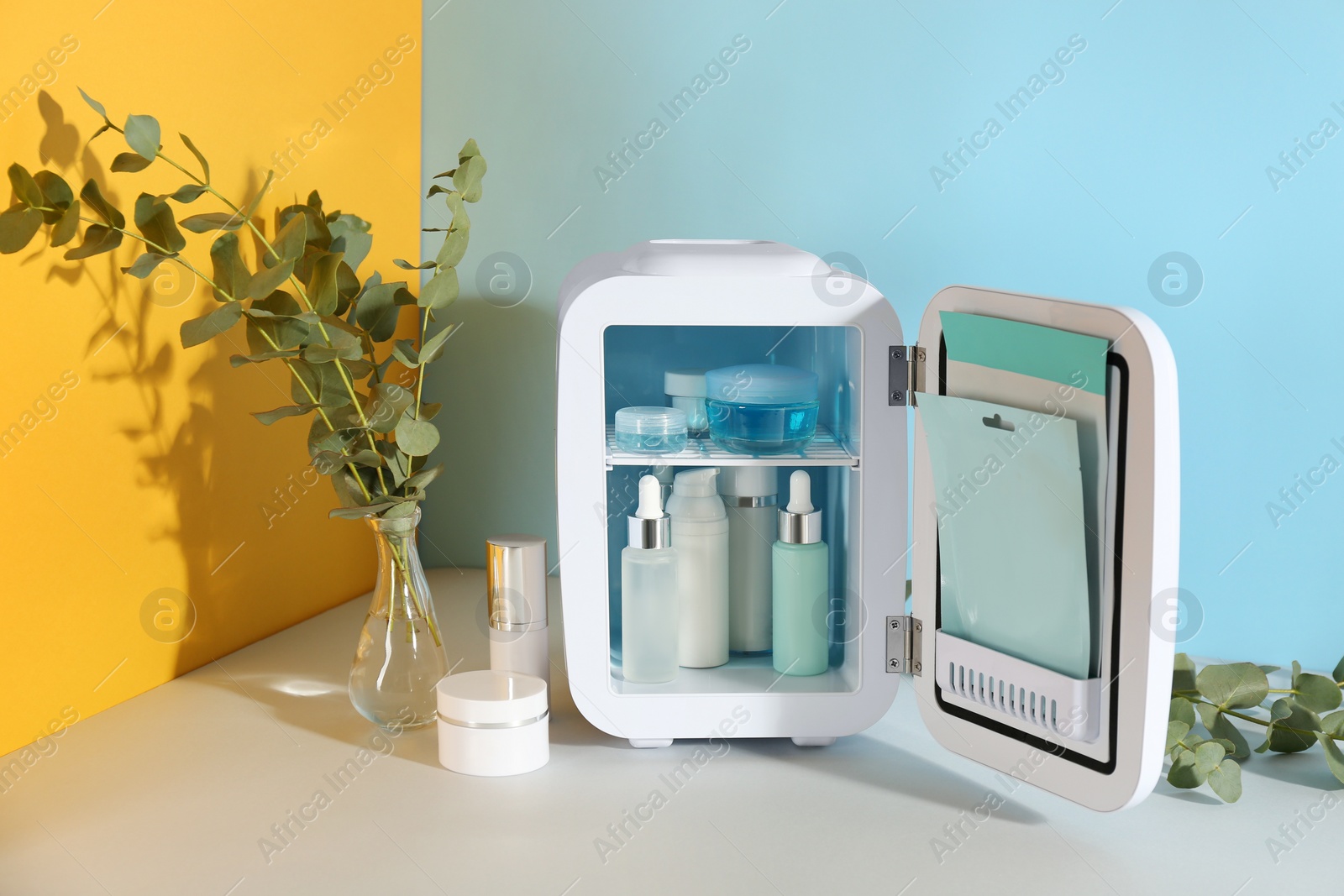 Photo of Open cosmetic refrigerator and skin care products on color background