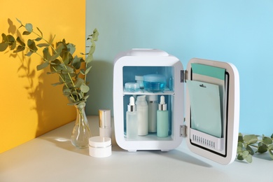 Photo of Open cosmetic refrigerator and skin care products on color background