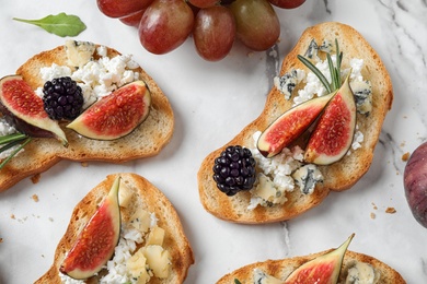 Photo of Bruschettas with cheese, figs and blackberries on white table, top view