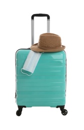 Stylish turquoise suitcase, hat and protective mask on white background. Travelling during coronavirus pandemic