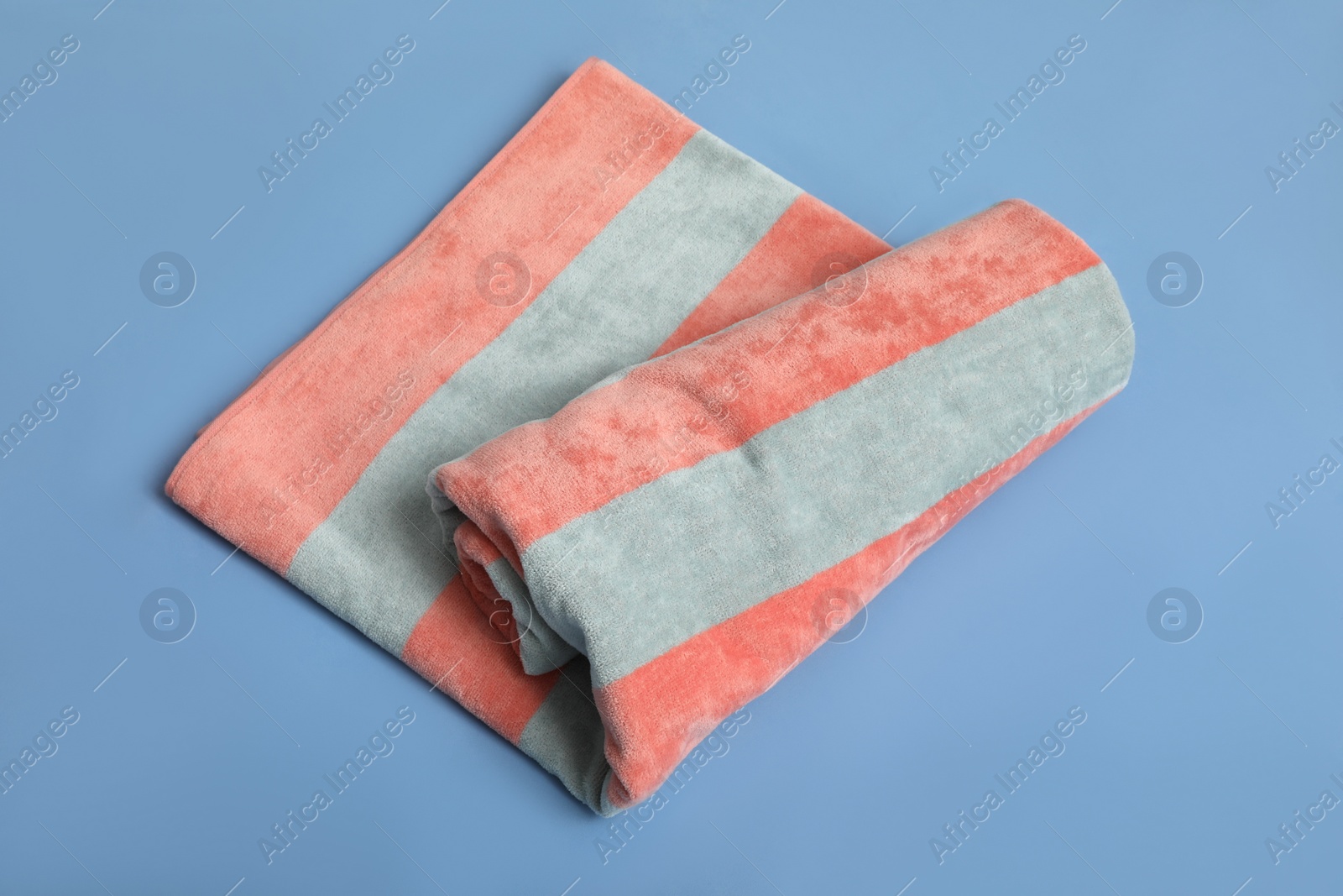 Photo of Rolled striped beach towel on blue background