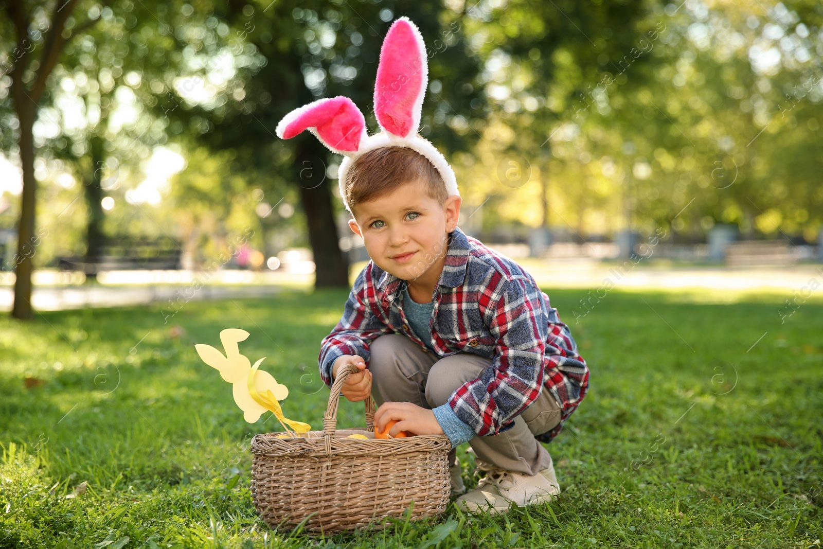 Photo of Cute little boy with bunny ears and basket of Easter eggs in park