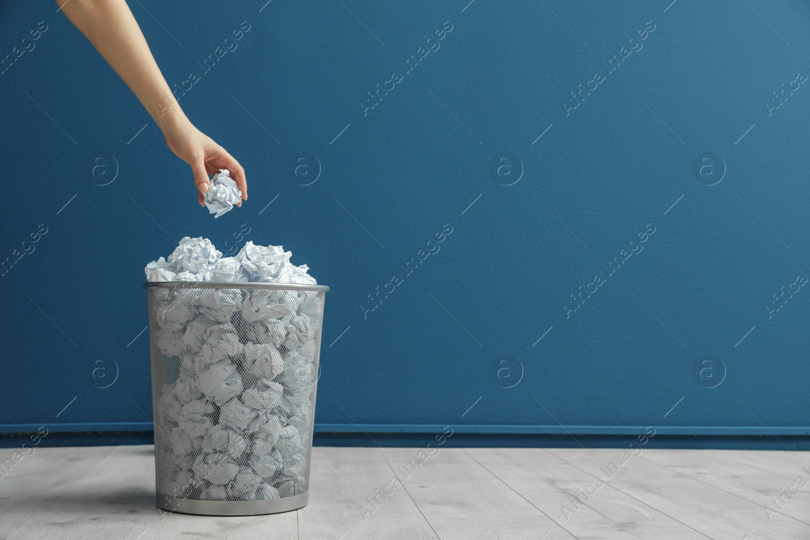 Photo of Woman throwing crumpled paper into metal bin against color wall. Space for text