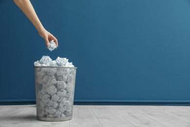 Photo of Woman throwing crumpled paper into metal bin against color wall. Space for text