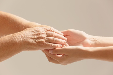 Photo of Helping hands on gray background, closeup. Elderly care concept