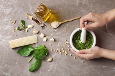 Photo of Woman mixing pesto sauce with pestle in mortar on grey table, flat lay