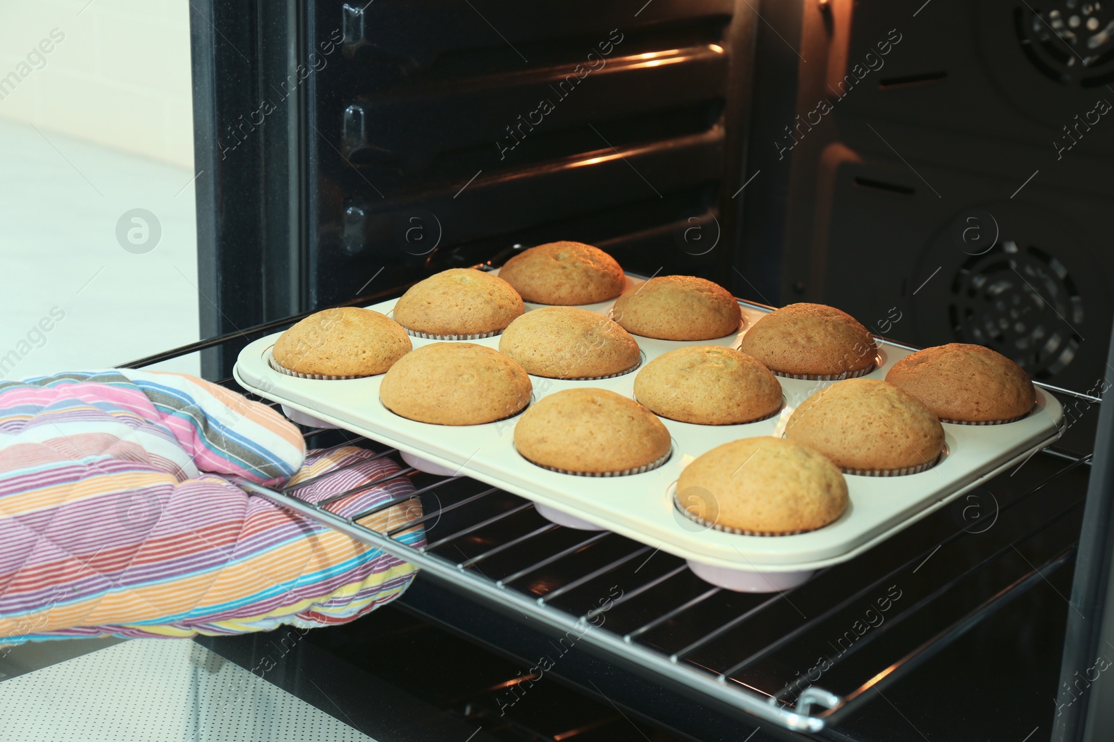 Photo of Woman taking cupcakes out of oven indoors, closeup