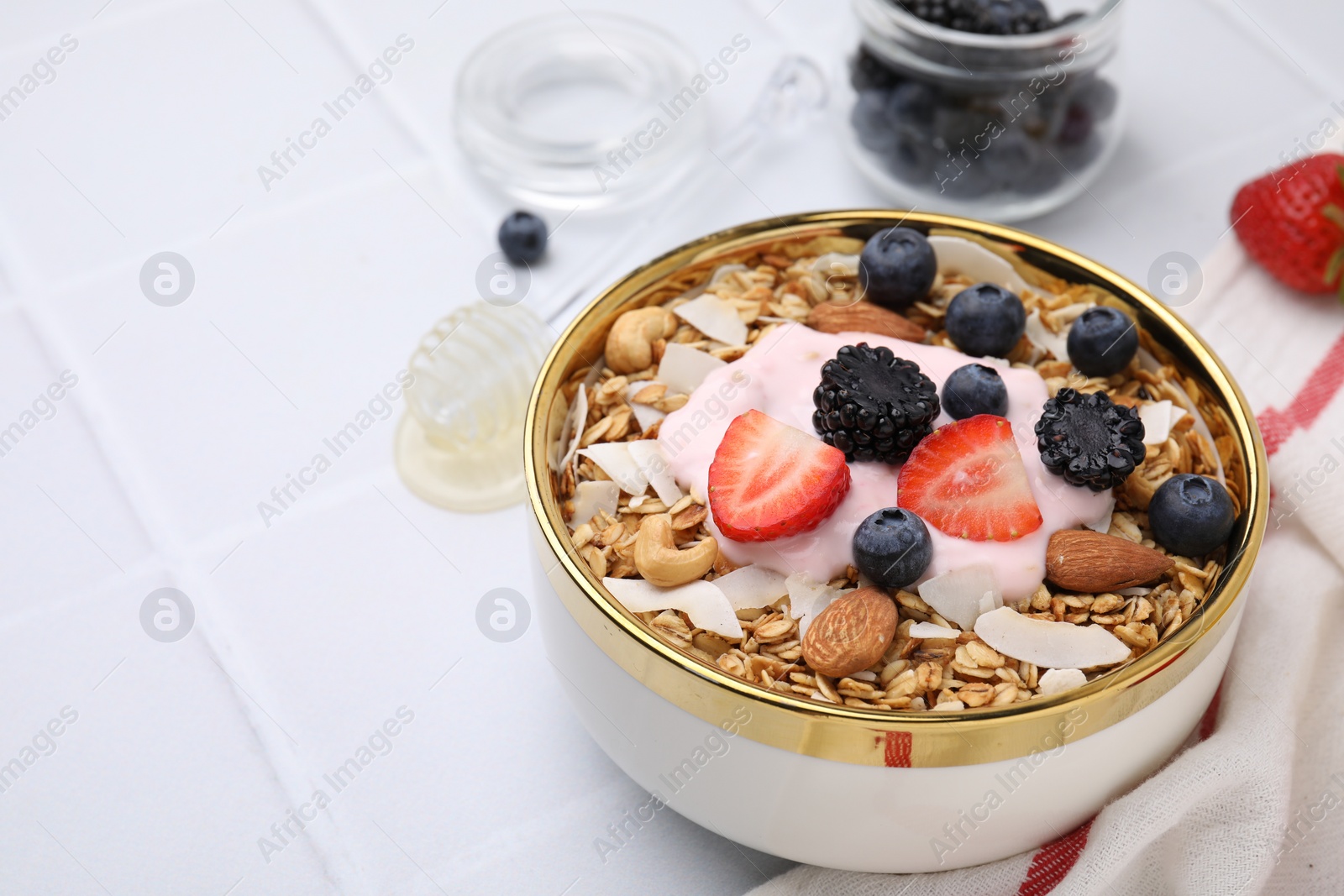 Photo of Tasty granola, yogurt and fresh berries in bowl on white tiled table, closeup with space for text. Healthy breakfast