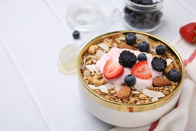 Photo of Tasty granola, yogurt and fresh berries in bowl on white tiled table, closeup with space for text. Healthy breakfast