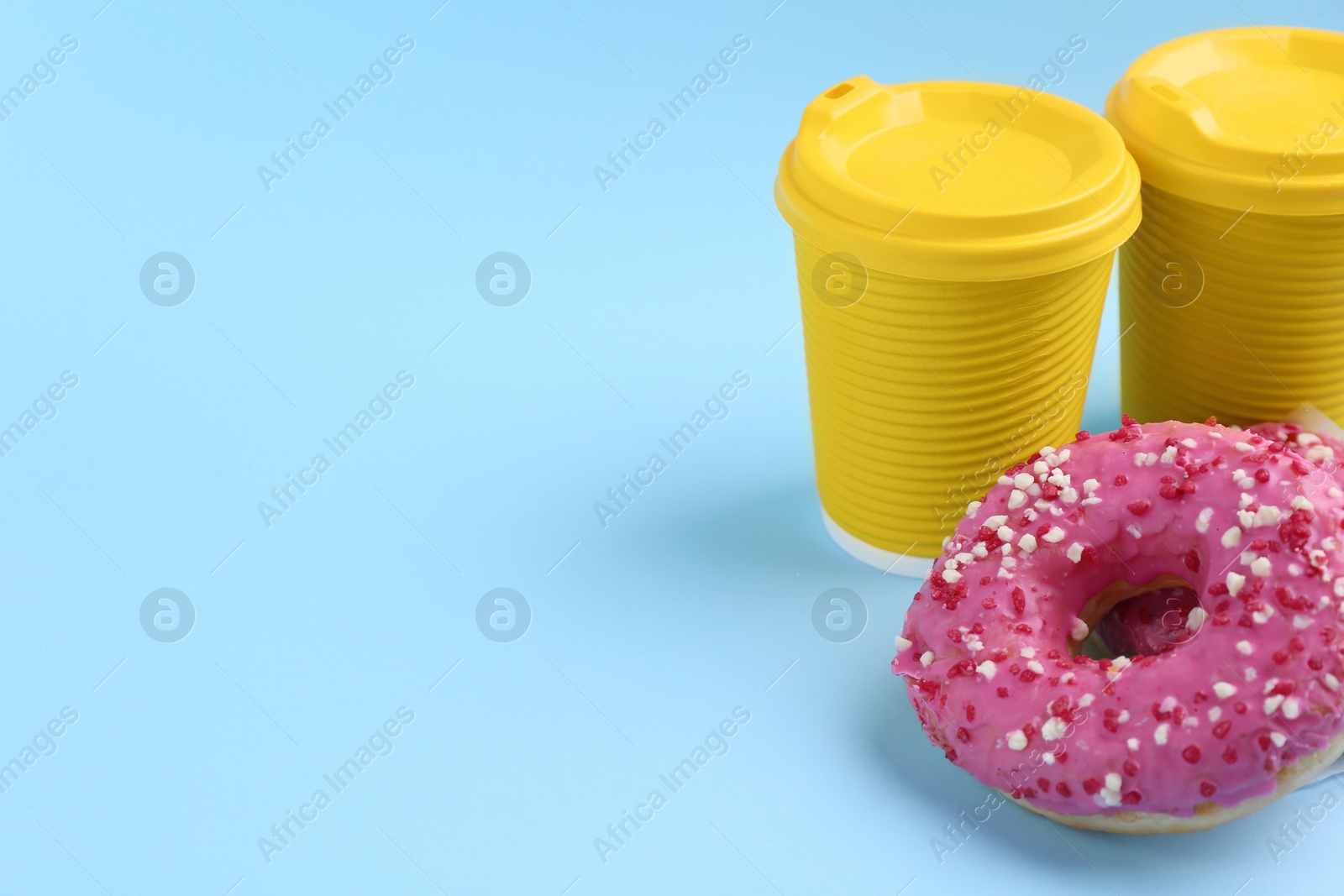 Photo of Delicious fresh donuts with sprinkles and hot drink in paper cups on light blue background, space for text