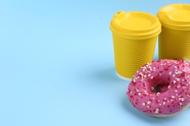 Delicious fresh donuts with sprinkles and hot drink in paper cups on light blue background, space for text