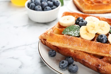 Photo of Delicious Belgian waffles with blueberries and banana on white marble table, closeup. Space for text