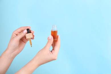 Photo of Woman applying essential oil onto wrist against light blue background, closeup. Space for text