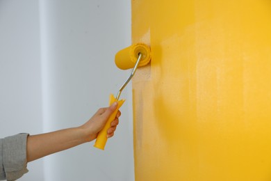 Woman painting white wall with yellow dye, closeup. Interior renovation