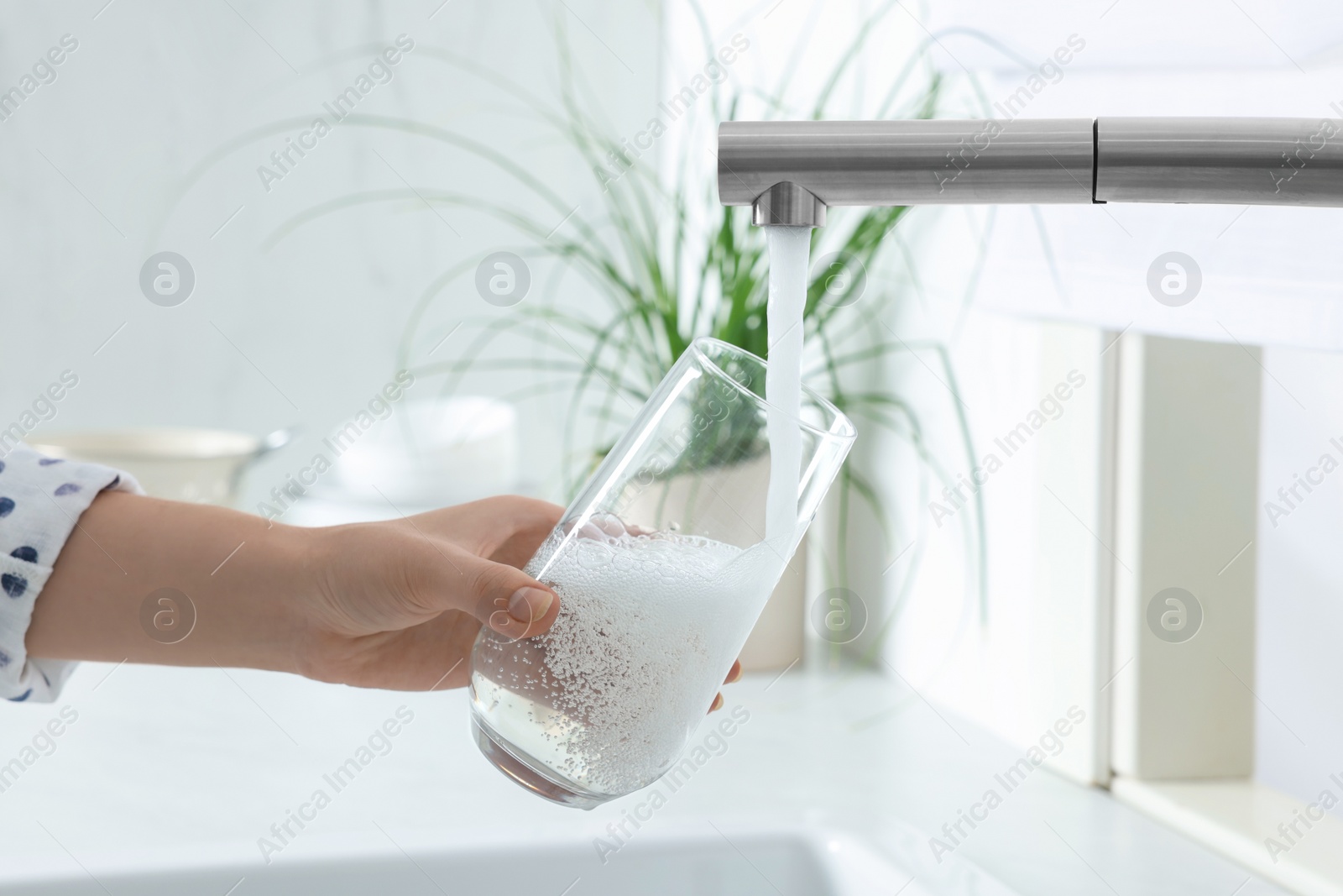 Photo of Woman filling glass with water from tap in kitchen, closeup