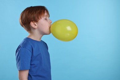Photo of Boy inflating yellow balloon on light blue background