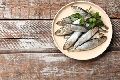 Photo of Fresh raw sprats and parsley on wooden table, top view. Space for text