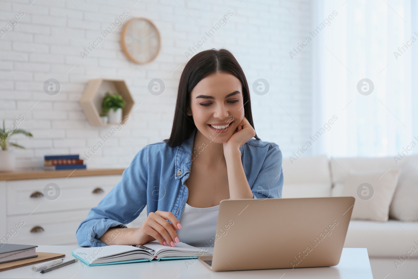 Photo of Young woman watching online webinar at table indoors