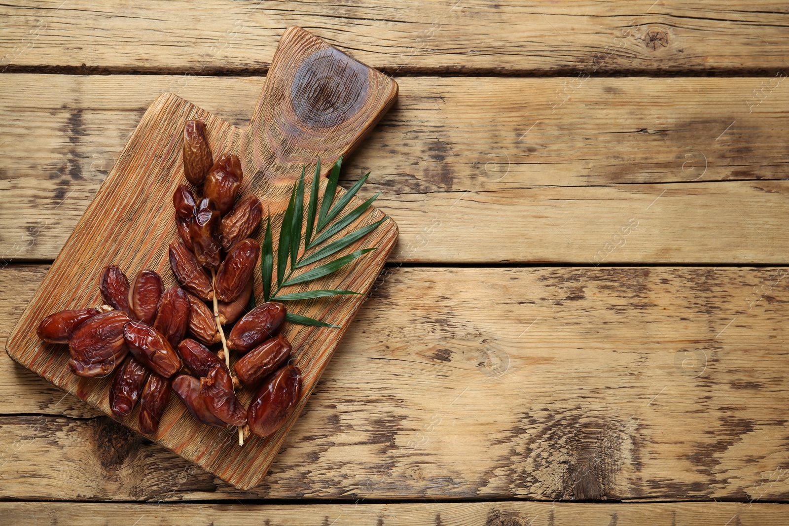 Photo of Sweet dried dates with green leaf on wooden table, top view. Space for text