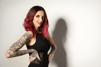 Photo of Beautiful woman with tattoos on body against light background. Space for text