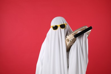 Photo of Person in ghost costume and sunglasses using retro radio receiver on red background, space for text