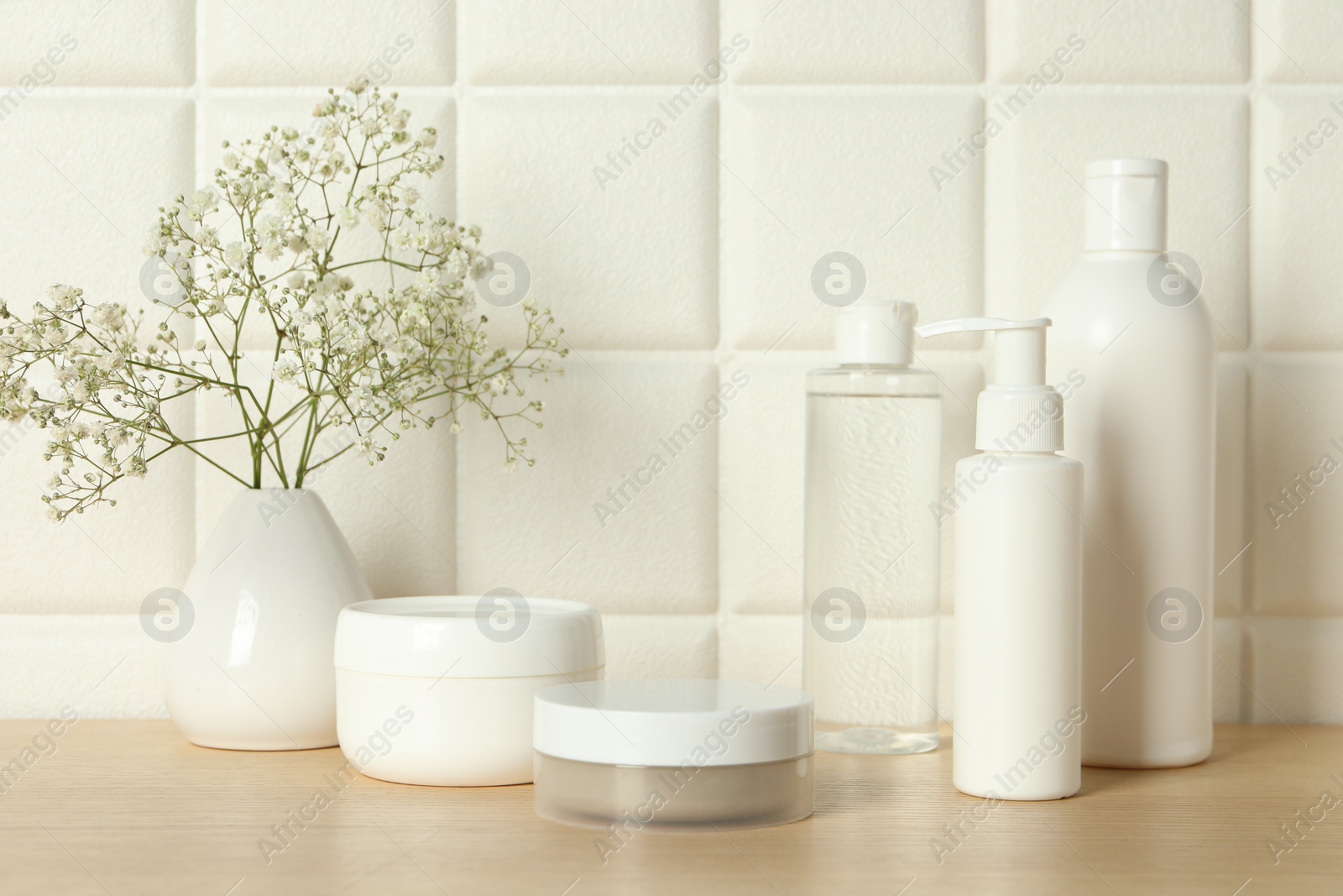 Photo of Bath accessories. Different personal care products and gypsophila flowers in vase on wooden table near white tiled wall