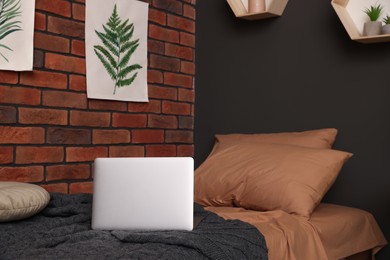 Stylish teenager's room with laptop on bed near brick wall