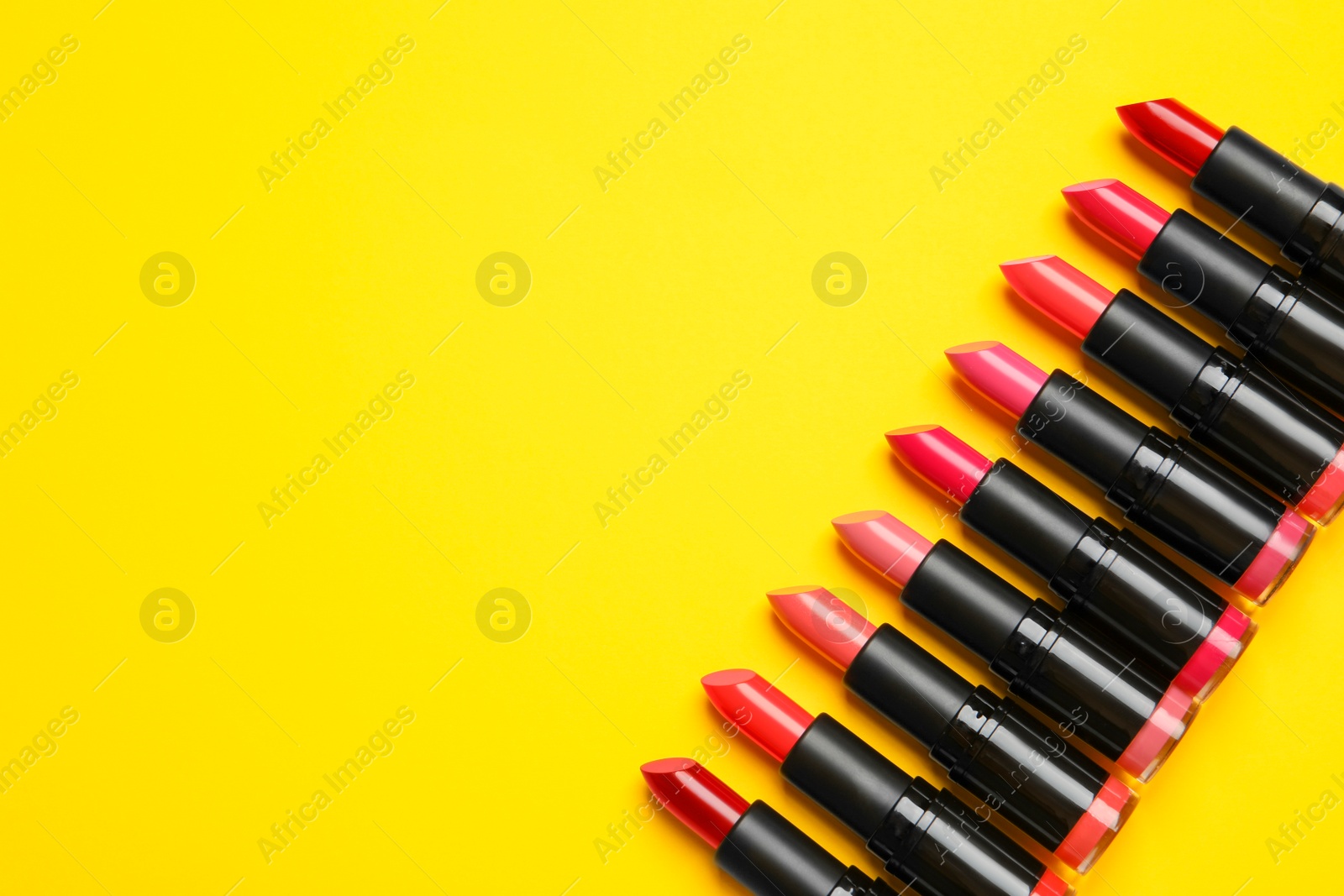 Photo of Many bright lipsticks on yellow background, flat lay. Space for text