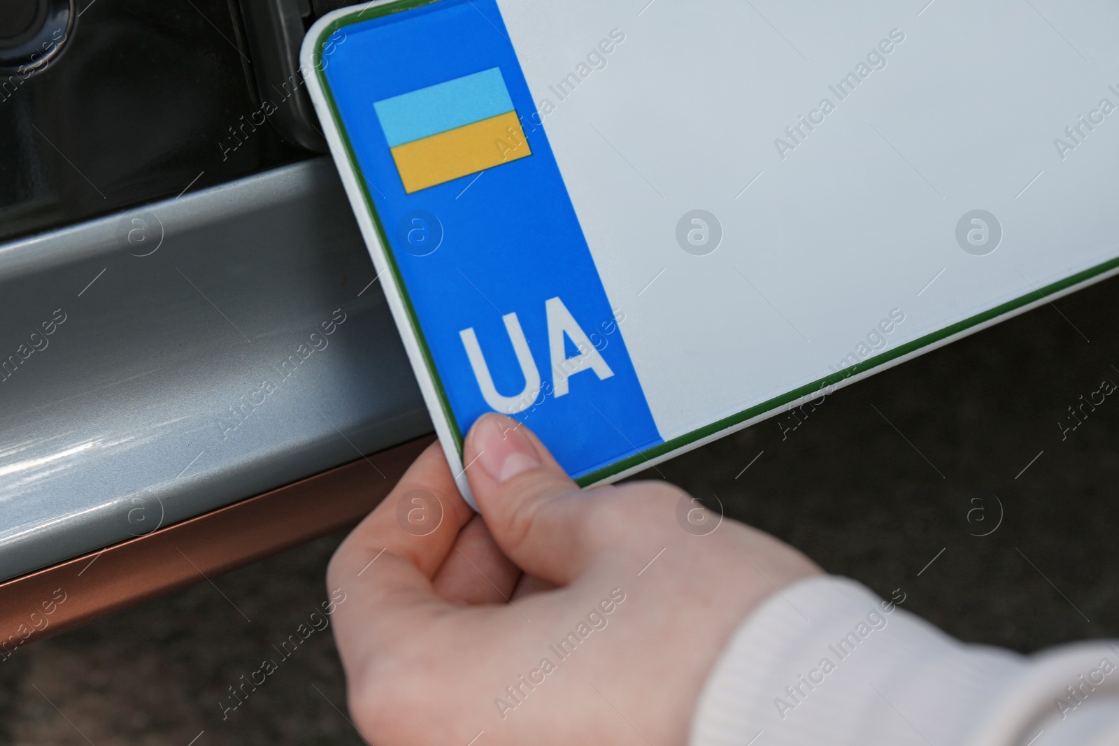 Photo of Woman installing vehicle registration plate outdoors, closeup