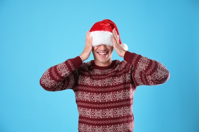 Photo of Young man in Christmas sweater and Santa hat on light blue background