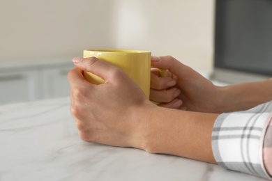 Photo of Woman with yellow cup at table indoors, closeup