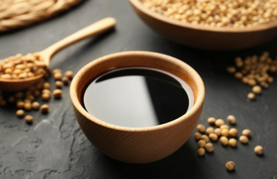 Photo of Tasty soy sauce in bowl and soybeans on black table, closeup