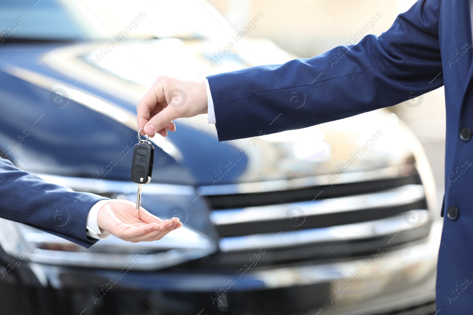 Photo of Salesman giving key to customer in modern auto dealership, closeup. Buying new car